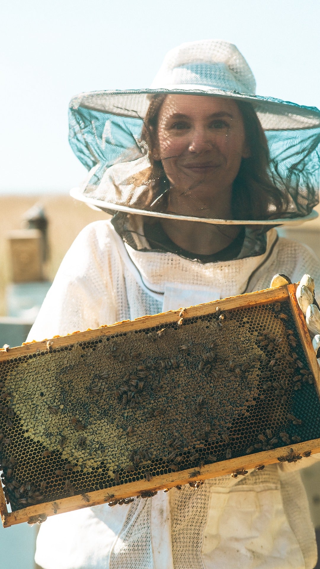 Beekeeeper and owner Rey Wilson wearing a beekeeping suit holding a honeycomb frame in the DMV